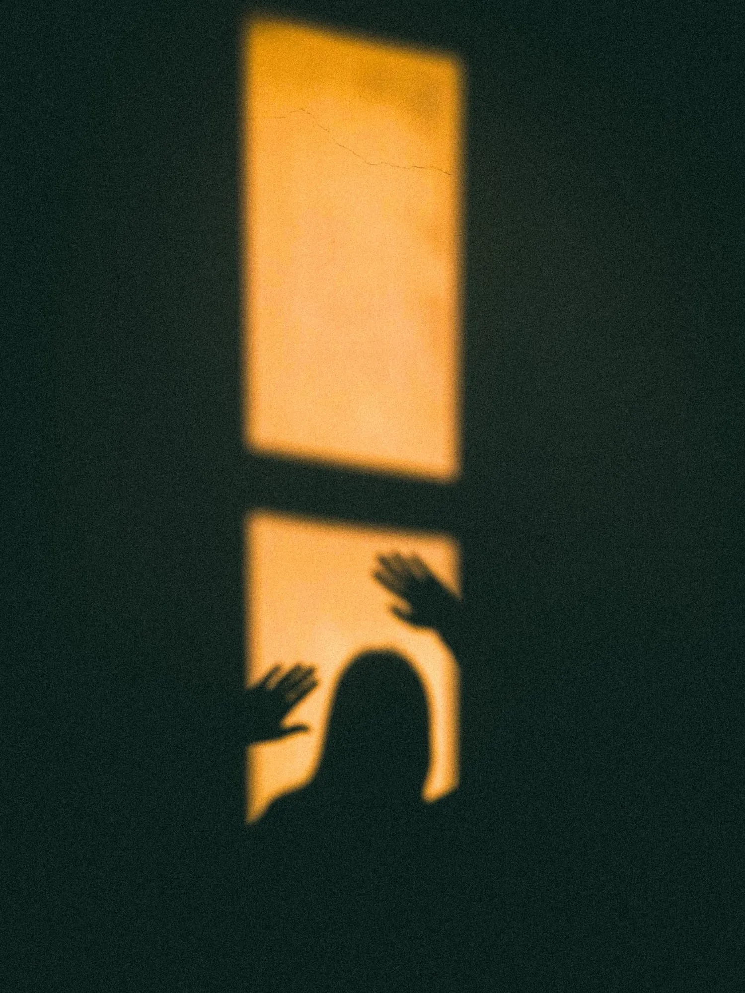 Schatten einer Person im warmen Fensterlicht auf dunkler Wand